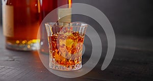 bartender puts ice cubes for cooling into a glass of whiskey on a background of bottles