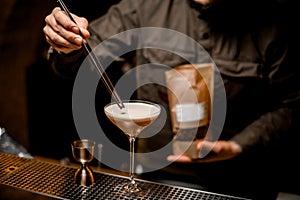 bartender s hand holds tweezers with coffee bean and decorates by it glass with frothy cocktail