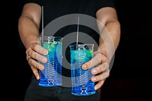 Bartender's hands serve 2 alcoholic cocktails with blue syrup blue lagoon in the black background