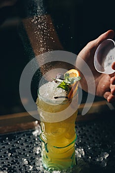 Bartender`s hands sprinkling the juice into the cocktail glass filled with alcoholic drink on the dark background
