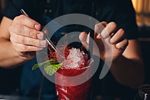 Bartender`s hands sprinkling the juice into the cocktail glass filled with alcoholic drink on the dark background