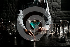 Bartender serving a blue alcoholic cocktail in a martini glass decorated with a dry spikelet