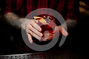 Bartender serving glass of a Boulevardier cocktail with orange zest on the bar counter