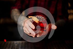 Bartender serving glass of a delicious Boulevardier cocktail with orange zest on the bar counter