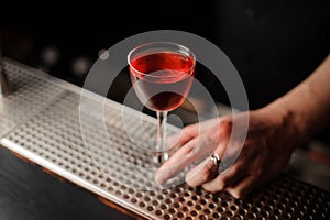 Bartender serving a transparent red cocktail in the glass on the steel bar counter