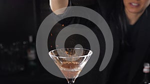 Bartender sets fire to cocktail, burning cinnamon in alcohol drink on black background. Flames in cocktail glass in slow