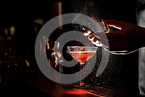 Bartender sprays an orange peel in cocktail glass