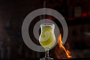 Bartender sprinkles on illuminated glass with bright green cold cocktail on bar counter and makes fire flame over it