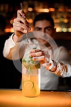 bartender stirring cocktail in bottle with long bar spoon on the bar