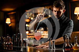 Bartender stirring the pink color alcoholic cocktail drink with a spoon in the glass