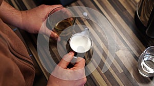 Bartender taps a milk jug with frothed milk and a glass of coffee on the table