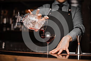 Bartender in a tie and apron pouring red alcoholic drink in a cocktail glass