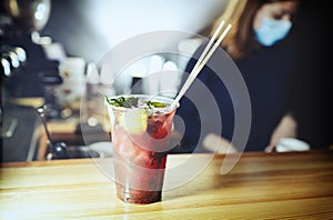 Bartender wearing face protection mask,making mojito cocktail. Process of bartending in bar.Mint leaves,ice,lime - ingredients for