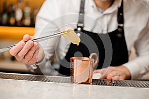 Bartender in white shirt adding two slices of ginger into a cup