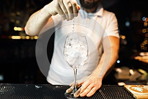 Bartender in white t-shirt at the bar or in a nightclub and makes an alcoholic cocktail. Lifestyle