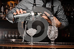 Bartenders hands pouring alcoholic drink into a glass using a jigger to prepare a cocktail