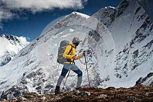 Barve solo hiker walking across high altitude mountain track. Traveler with backpack and trekking poles climb up to mountains rock