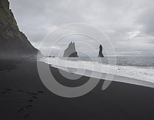 Basalt rock formations Troll toes on black sand beach reynisfjara with group of colorful tourist people, fog and moody