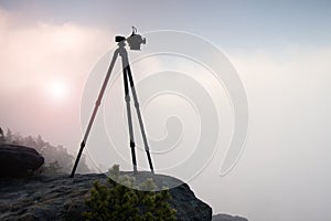 Basalt tripod with professional camera on the peak ready for photography. Sandstone peaks increased from gold foggy background