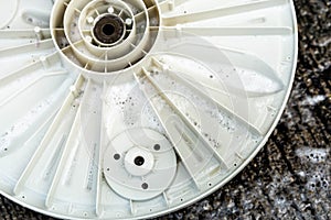 The base plate of the washing machine drum is soiled on a cement floor, removed for cleaning