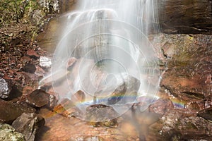 Base of a powerful waterfall splashing on the rock creating a rainbow