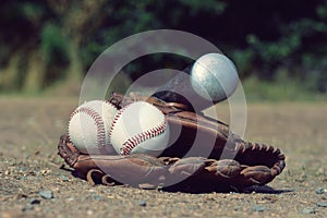 Baseball ball in leather glove with a baseball bat lying on the playground