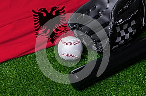 Baseball bat, glove and ball near Albania flag on green grass background