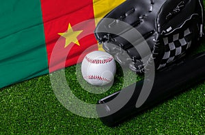 Baseball bat, glove and ball near Cameroon flag on green grass background
