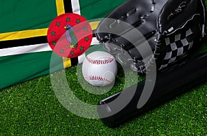 Baseball bat, glove and ball near Dominica flag on green grass background