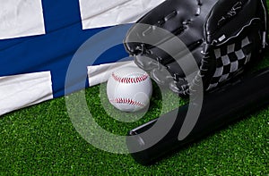 Baseball bat, glove and ball near Finland flag on green grass background