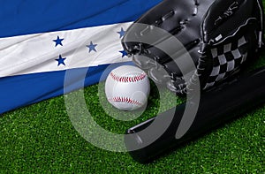 Baseball bat, glove and ball near Honduras flag on green grass background