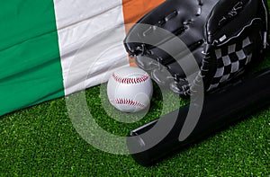 Baseball bat, glove and ball near Ireland flag on green grass background