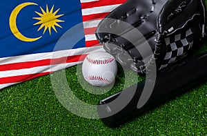 Baseball bat, glove and ball near Malaysia flag on green grass background