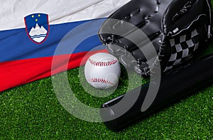Baseball bat, glove and ball near Slovenia flag on green grass background