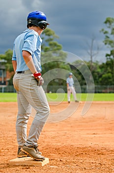Baseball game, runner on the third base is watching the pitcher and getting ready to run to home plate and score