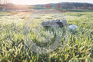 Baseball glove and ball on grass field with sun rising