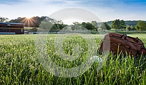 Baseball and glove on grass in morning dew near dugout early spring