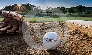 Baseball and glove on pitcher`s mound in early morning