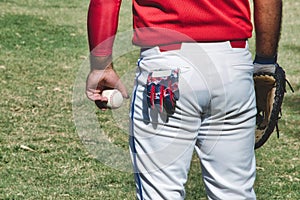 A baseball player at a match wearing a leather mitt and holding a ball in his hand, with a glove sticking out of his pocket