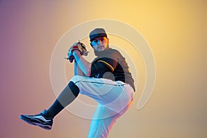 Baseball player, pitcher in a black uniform practicing on gradient background in neon light