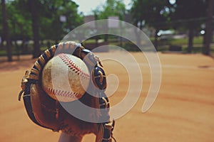 Baseball season ball and glove close up with field in background.