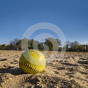Baseball softball on the sand diamond area with grass and trees in the distance