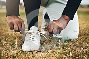 Baseball, sports and shoes with a man athlete tying his laces on a grass pitch or field for training or a game. Fitness