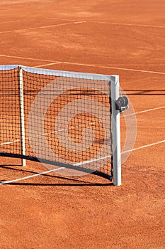 Baseline and net of an empty clay tennis court on a sunny day