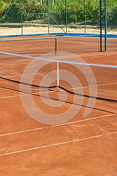 Baseline and net of an empty clay tennis court on a sunny day