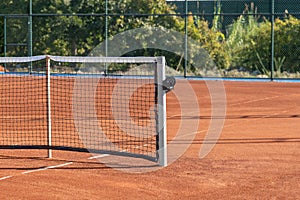 Baseline and net of an empty clay tennis court on a sunny day