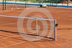 Baseline and net of an empty clay tennis court on a sunny day