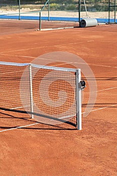 Baseline and net of an empty clay tennis court on a sunny day