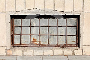 Basement window made of strong frame with metal bars and sheet metal filling mounted on house wall locked with rusted padlock