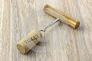 A basic corkscrew with a cork on a wooden table. Tokaji is wine`s name written on cork from Tokaj wine region